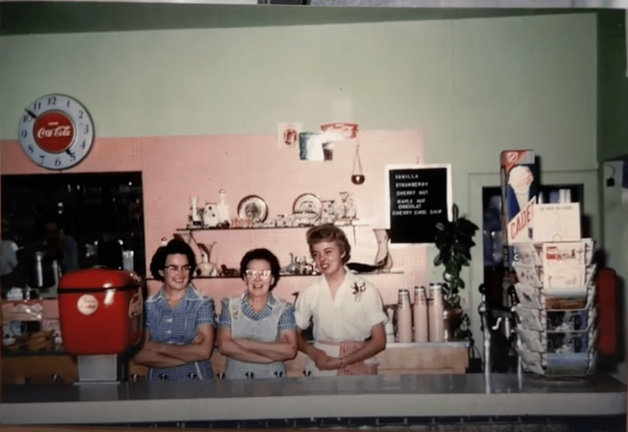 Three fountain staff behind the soda counter, Coca-Cola clock on the wall